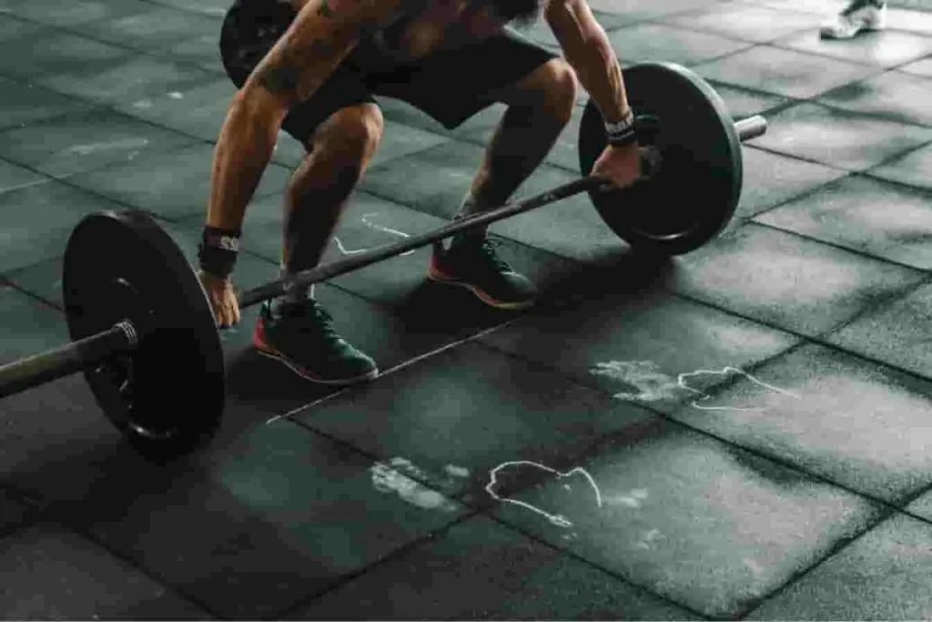Personne en position basse avec jambes tendues et barre chargée au sol sur sol en dalles, image qui évoque un soulevé de terre roumain