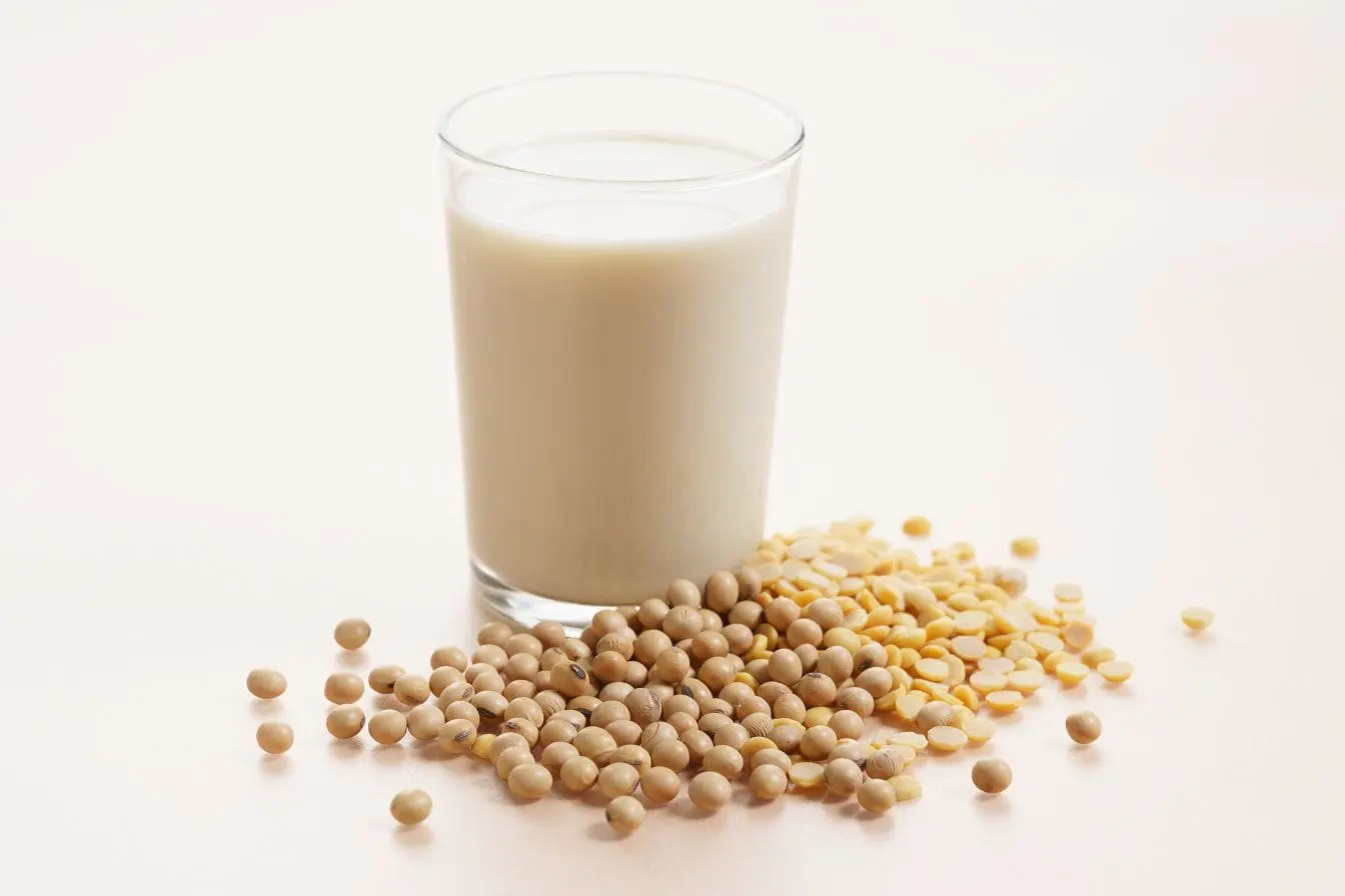 Verre de lait blanc posé sur surface claire avec graines de soja entières et lentilles jaunes en avant-plan