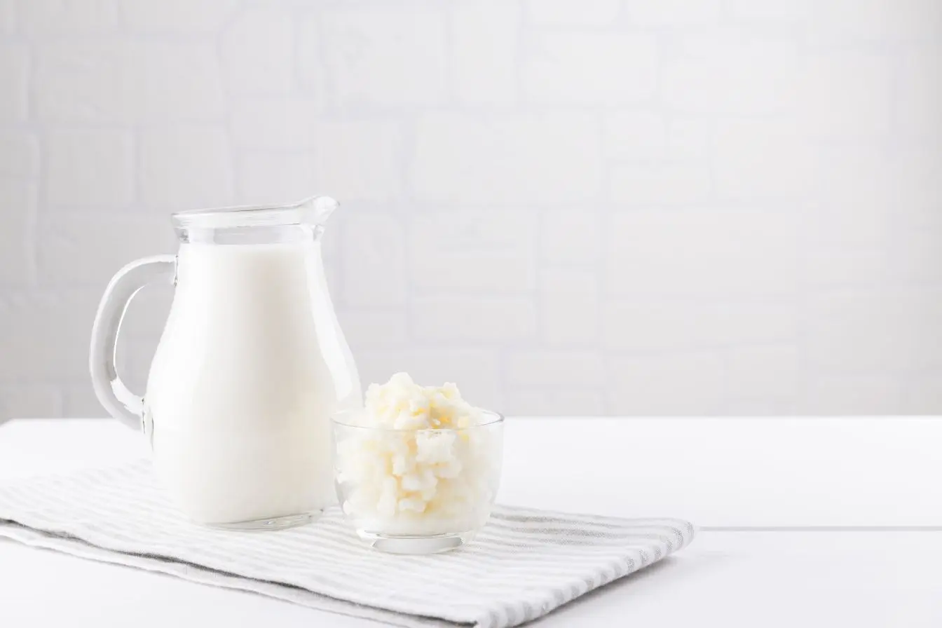 Pichet de lait et bol de grains fermentés posés sur une nappe claire, évoquant les bienfaits des laits fermentés sur la santé
