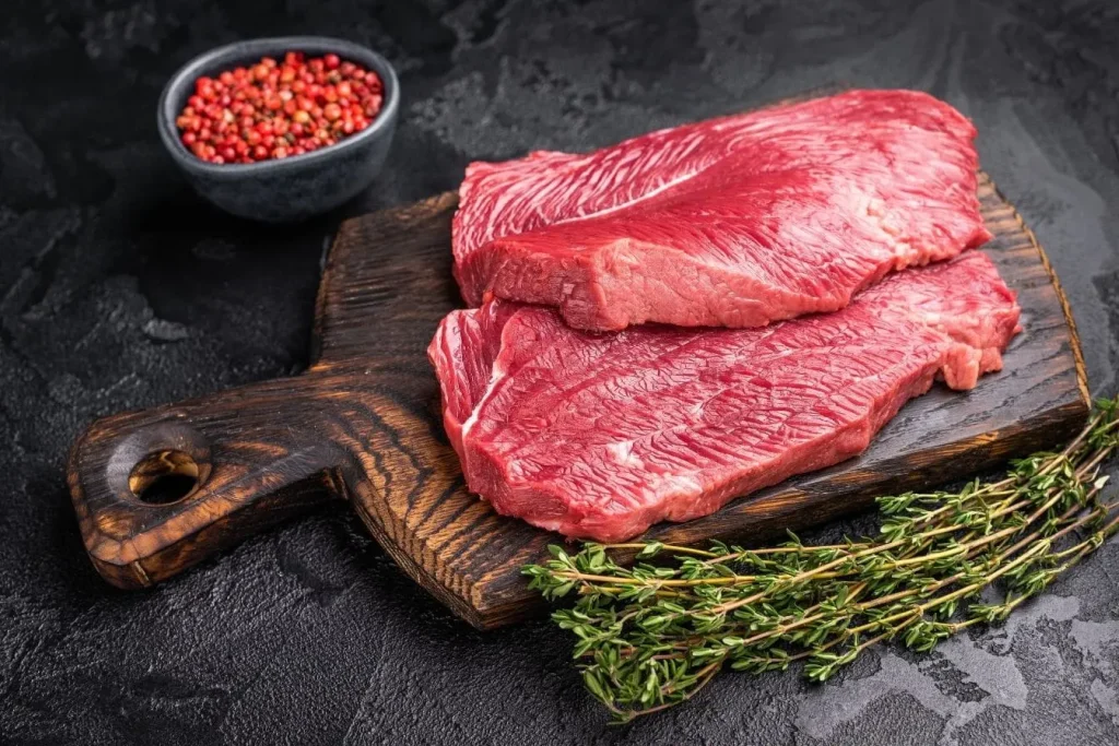 Deux pièces de viande rouge crue sur planche en bois illustrant un aliment à limiter en cas de goutte