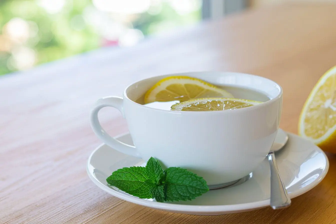 Tasse blanche avec eau citronnée et menthe illustrant une boisson détox pour digestion et hydratation