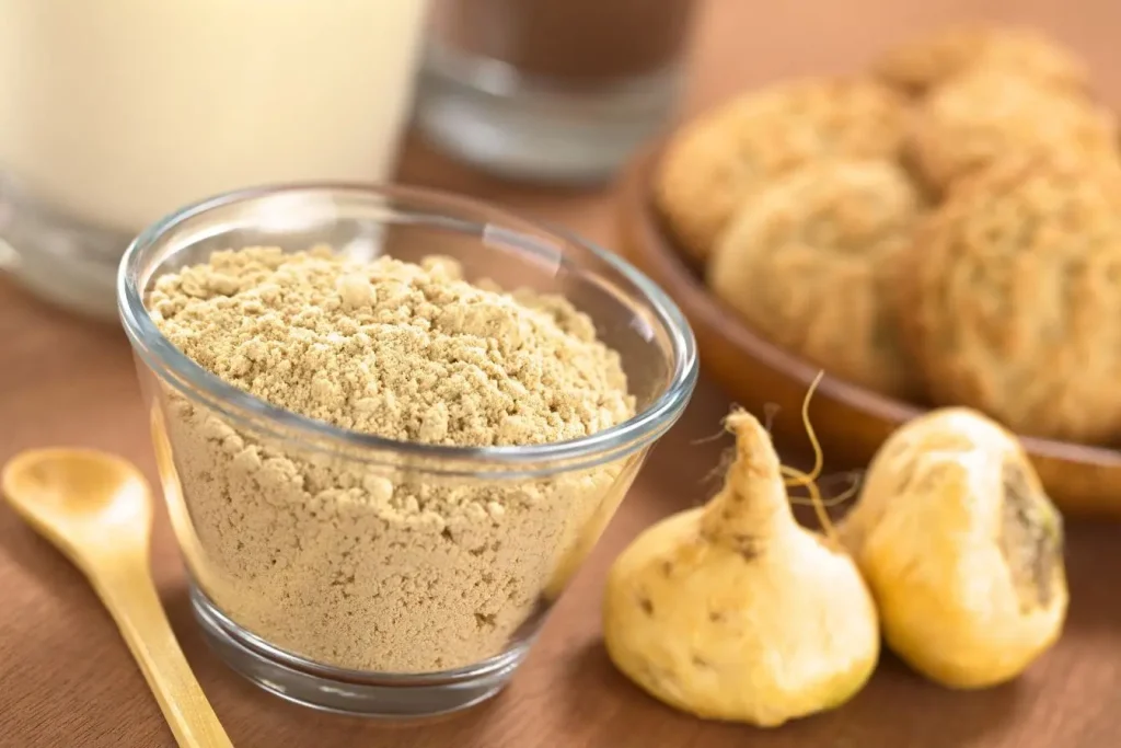 Poudre de maca du Pérou dans un bol en verre avec racines entières et cuillère en bois sur table