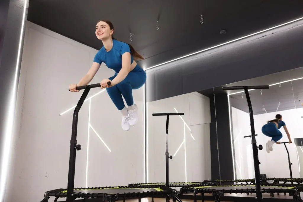 Personne en tenue bleue saute sur mini trampoline avec guidon, image illustrant le fitness dynamique et ludique en studio moderne