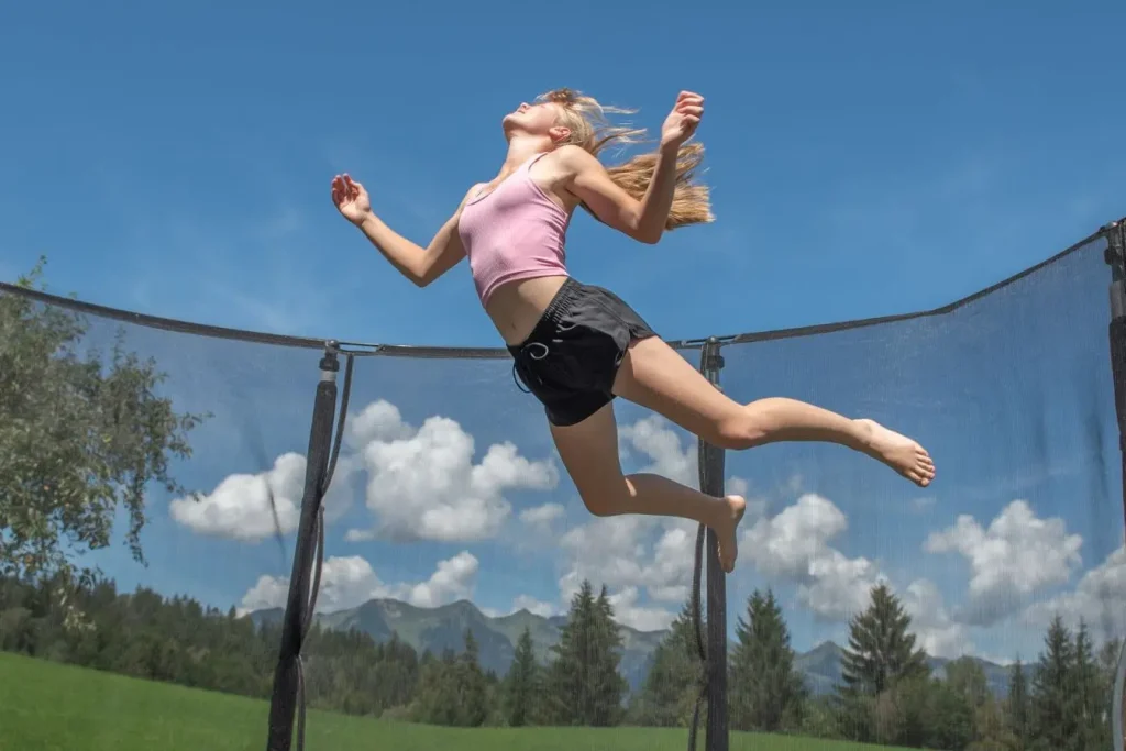 Personne en tenue sportive rose saute sur trampoline entouré de filet, image illustrant le fitness dynamique et ludique en plein air