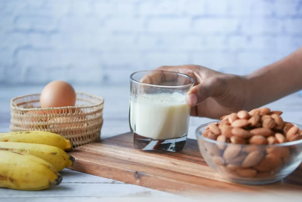 Banane mûre, verre de lait et amandes sur table en bois, image illustrant les aliments à privilégier pour apaiser le SPM naturellement.