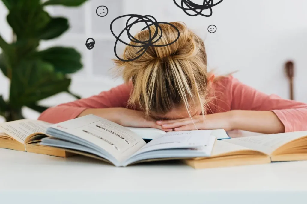Une jeune fille repose sa tête sur des livres ouverts avec des gribouillis noirs au-dessus de sa tête, brouillard mental qui peut être un signe de dysbiose intestinale.