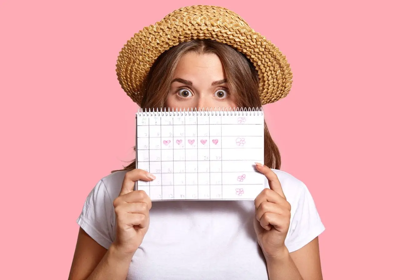 Personne cache visage derrière calendrier marqué de cœurs, image évoquant le suivi du cycle et l’importance des aliments à privilégier pour apaiser le SPM.