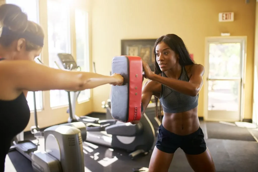 Sportive frappant un bouclier de frappe en salle illustrant la boxe française comme entraînement efficace pour brûler des calories.
