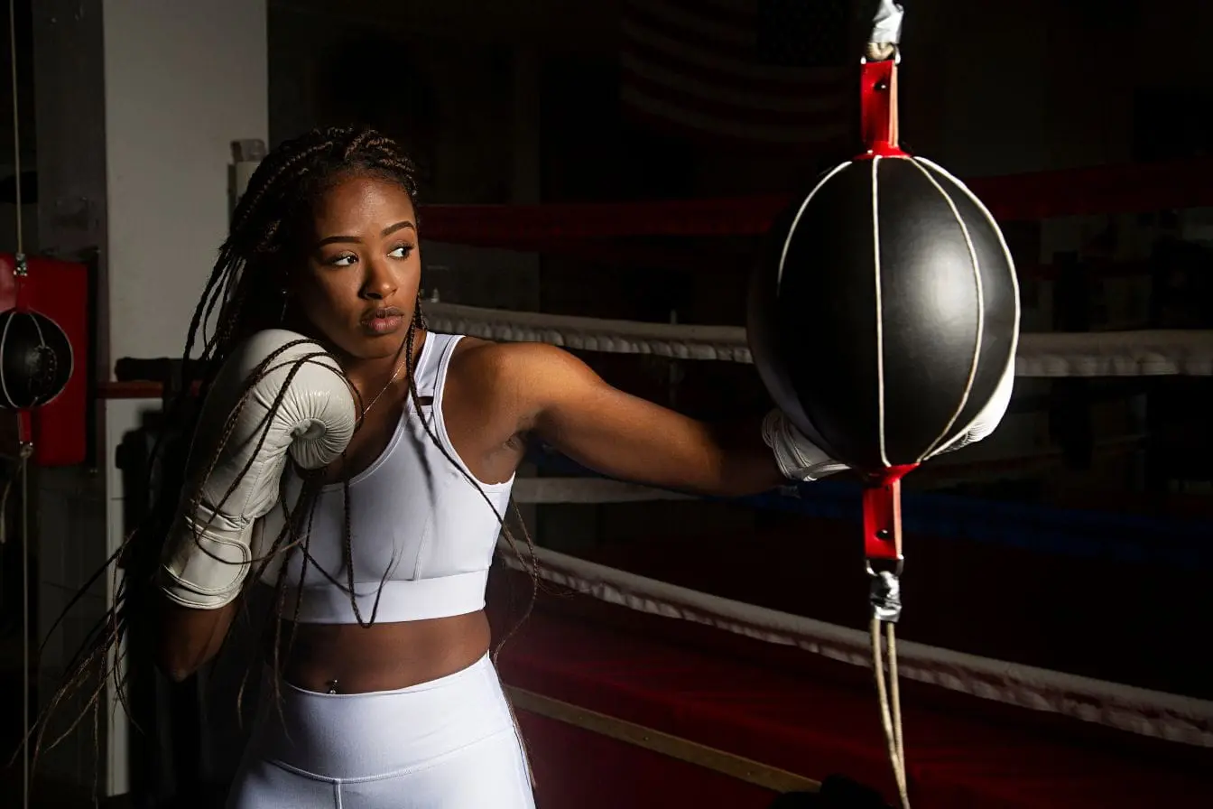 Sportive en tenue blanche frappant un sac double en salle de boxe illustrant l’efficacité de la boxe française pour brûler des calories