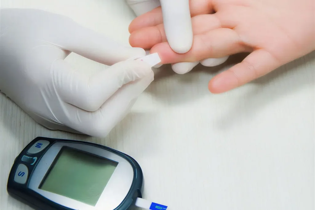 Gros plan sur doigt piqué avec bandelette insérée par mains gantées illustrant contrôle de la glycémie avec appareil posé à proximité