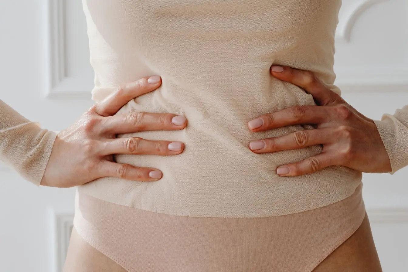 Une femme compresse son ventre avec ses mains pour exprimer une douleur abdominale, illustrant l'inconfort lié à une dysbiose intestinale chronique.