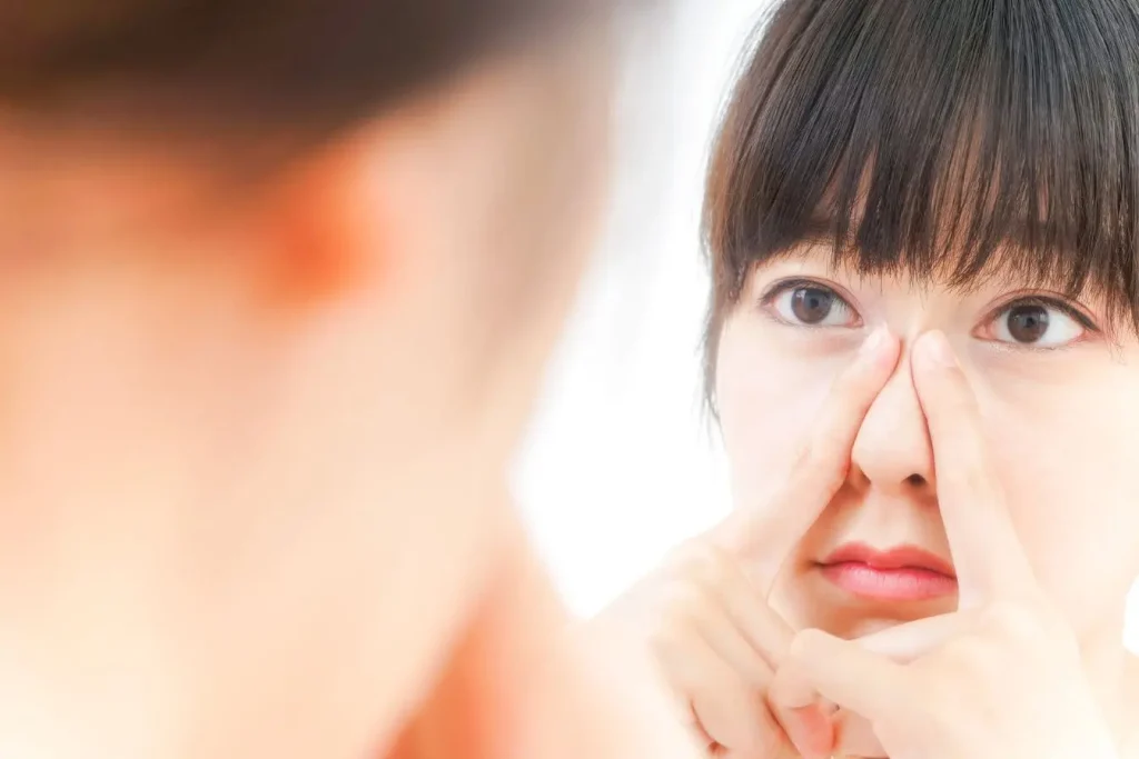Personne devant un miroir pinçant l’arête du nez avec les index, image illustrant un exercice de yoga du visage pour détente et tonus facial
