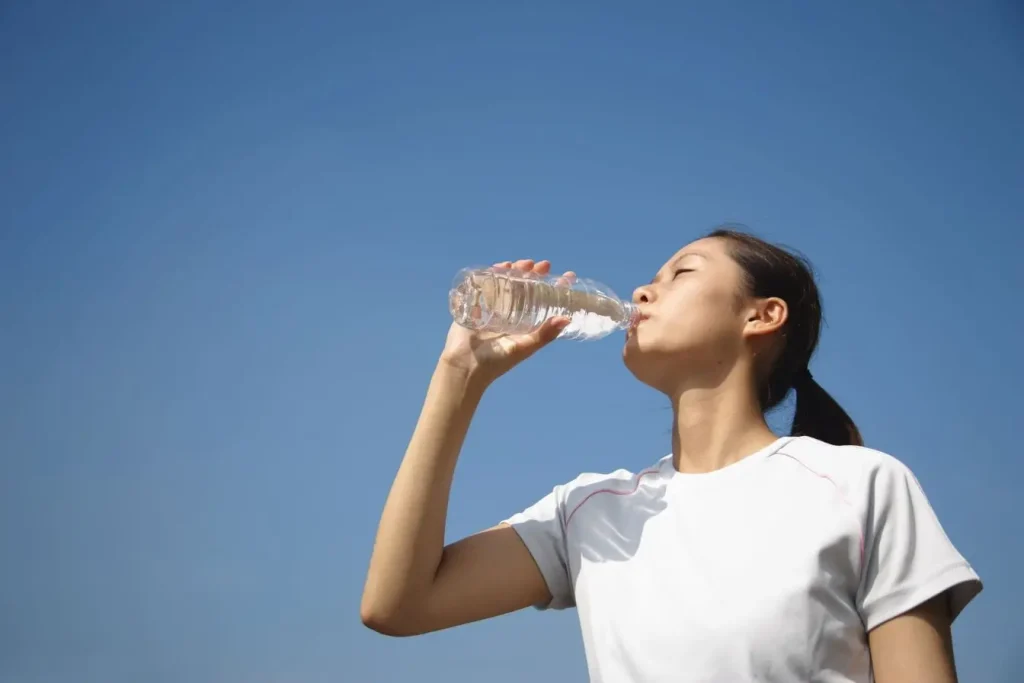 Personne en chemise blanche boit eau sous ciel bleu, image illustrant l’importance de l’hydratation parmi les aliments à privilégier pour apaiser le SPM.
