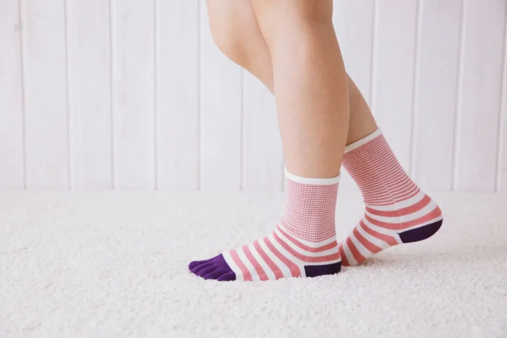 Personne debout sur tapis moelleux avec chaussettes rayées, symbole du repos et du soulagement des jambes lourdes.