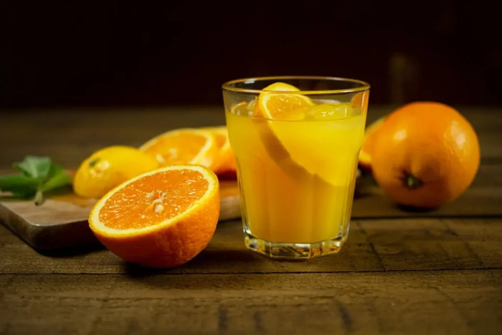 Verre de jus d’orange frais entouré de citrons et oranges, image illustrant la chrononutrition qui recommande les fruits le matin pour énergie et vitalité.
