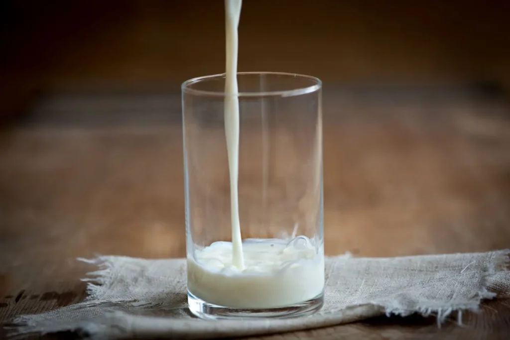 Un filet de kéfir de lait onctueux est versé dans un verre transparent posé sur une nappe en lin rustique pour une boisson probiotique saine.