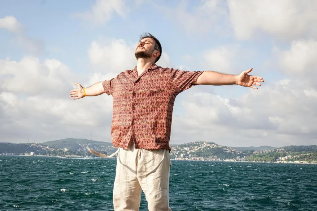 Personne debout bras ouverts face à l’eau, image illustrant la cohérence cardiaque comme pratique d’harmonisation entre souffle, rythme et équilibre intérieur.