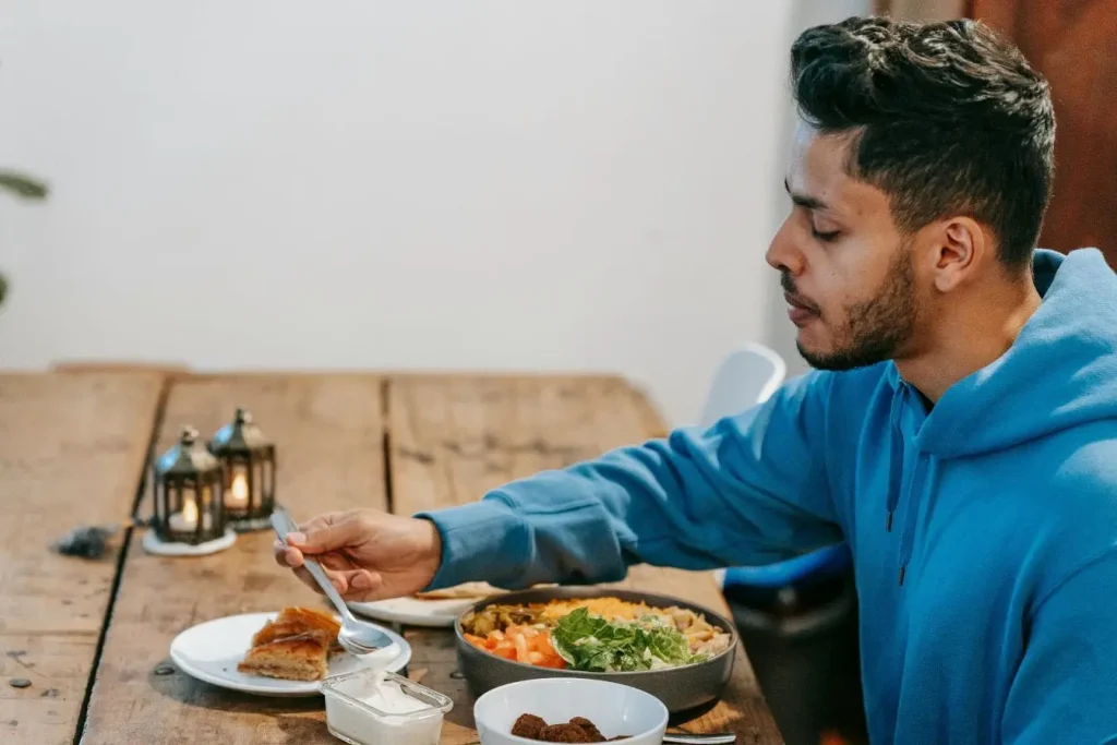 Personne en hoodie bleu mange repas varié avec salade et falafel, image illustrant distinction entre faim biologique et appétit lié au plaisir gustatif.