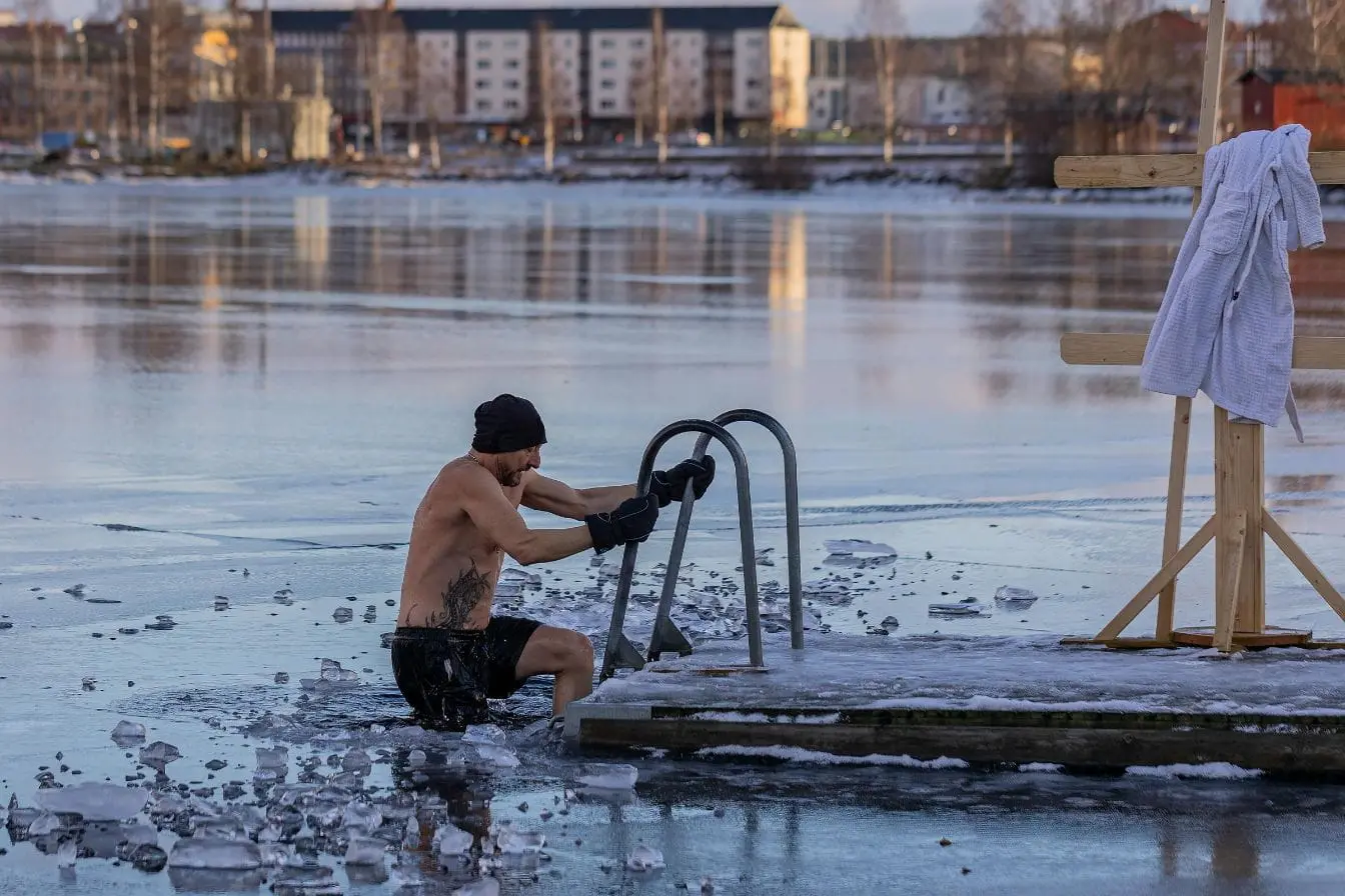 Personne descendant échelle vers eau glacée entourée de glace, image illustrant le bain froid utilisé pour favoriser la récupération musculaire.