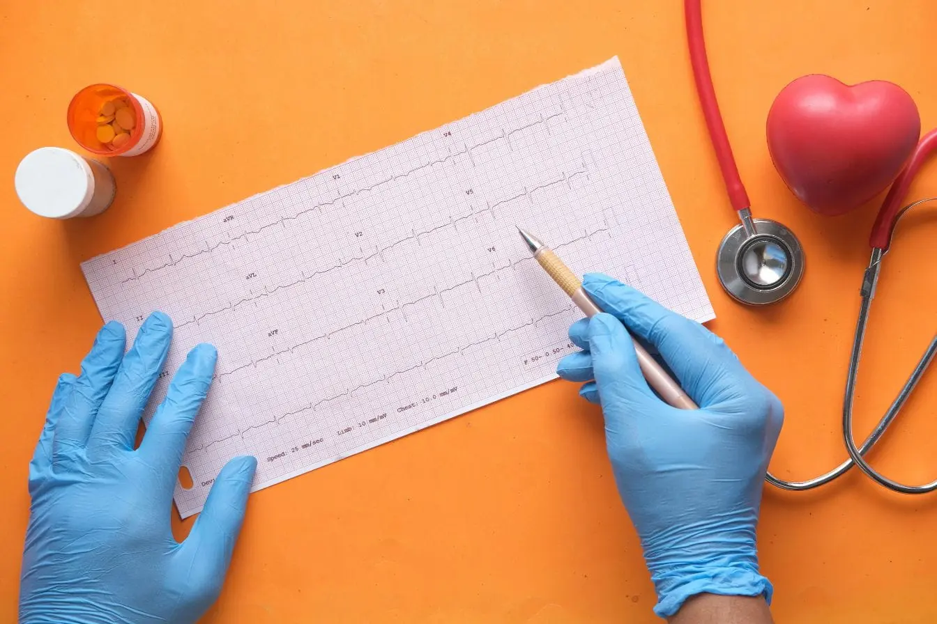 Mains gantées tenant tracé ECG avec stylo, image illustrant la cohérence cardiaque comme pratique de régulation du rythme et de la respiration.