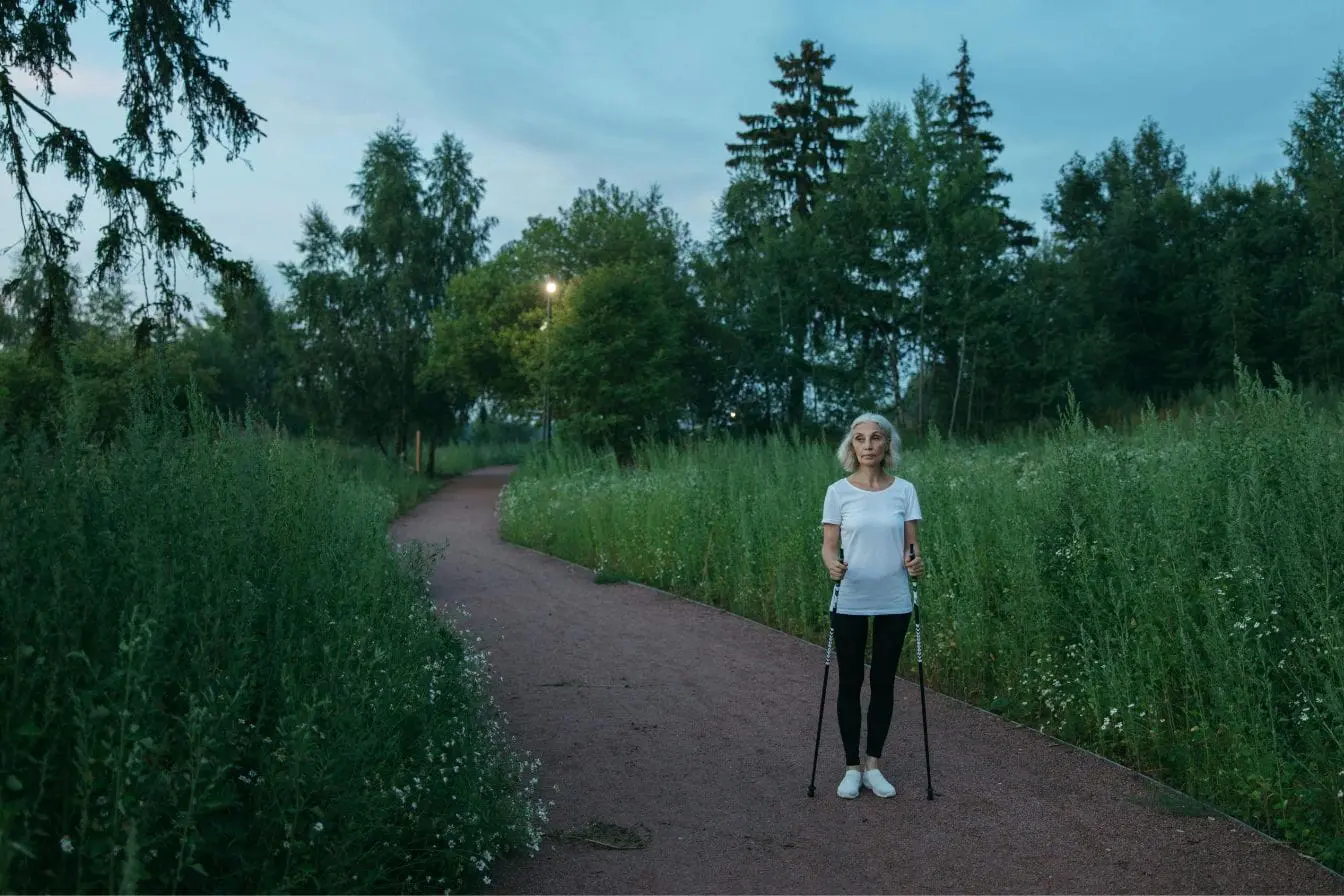 Personne marchant sur chemin entouré de verdure avec bâtons de marche, image illustrant la marche nordique et l’activité physique en plein air.