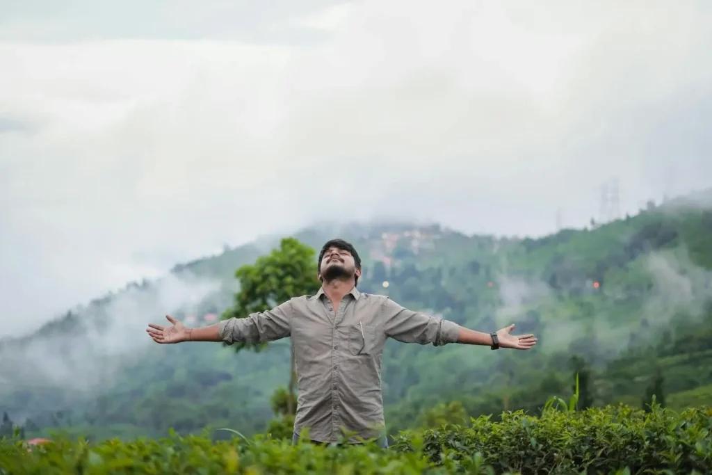 Personne debout bras ouverts dans paysage verdoyant, image illustrant la respiration abdominale pour relier souffle et équilibre intérieur.