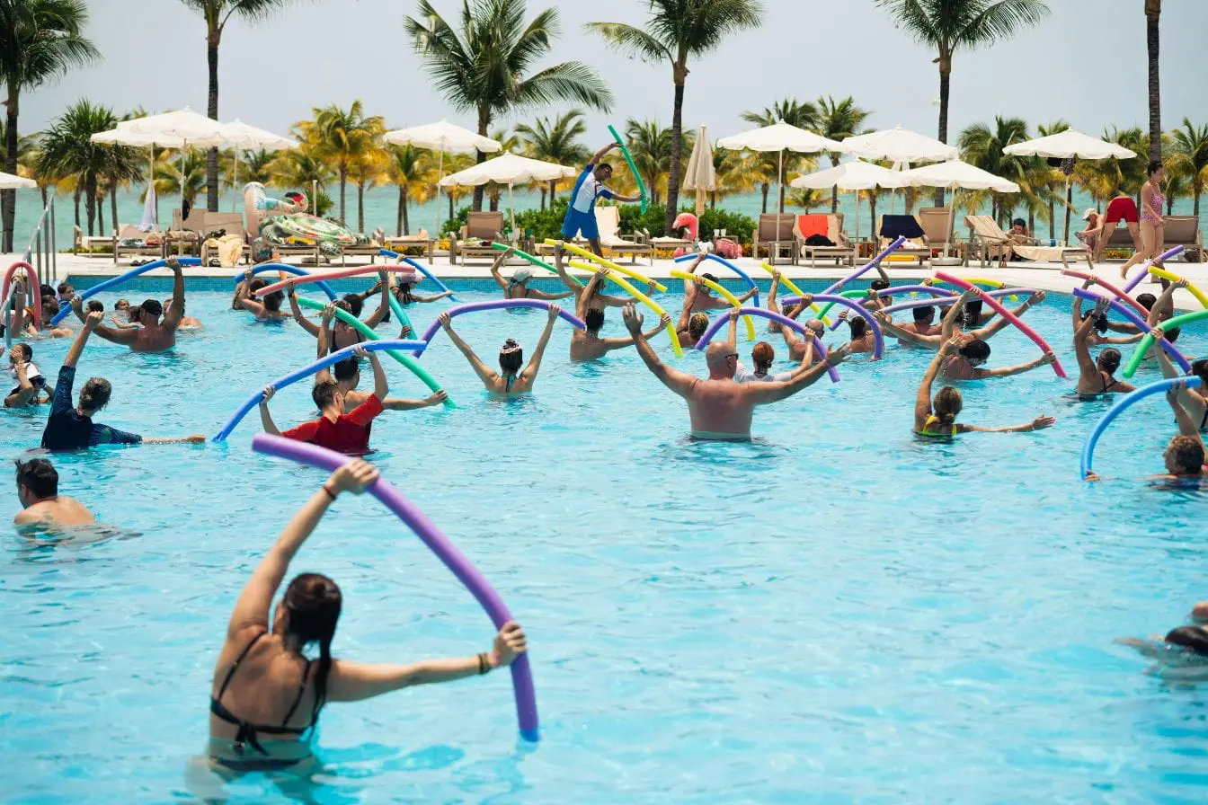 Groupe de personnes dans piscine suivant exercices avec frites colorées, image illustrant aquagym et calories brûlées dans ambiance sportive.