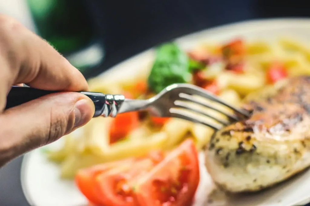 Main tenant une fourchette au-dessus d’un repas composé de poulet et légumes illustrant les choix alimentaires sains pour préserver le foie.