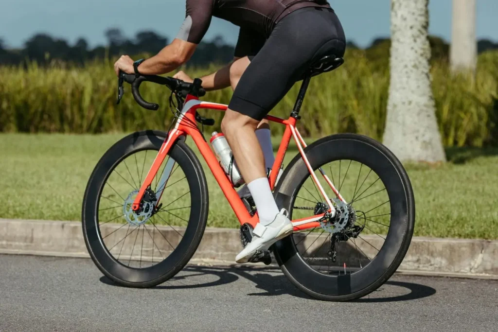 Cycliste en tenue sombre pédalant sur vélo rouge, image représentant les muscles sollicités lors du vélo de route et leur rôle dans l’effort.