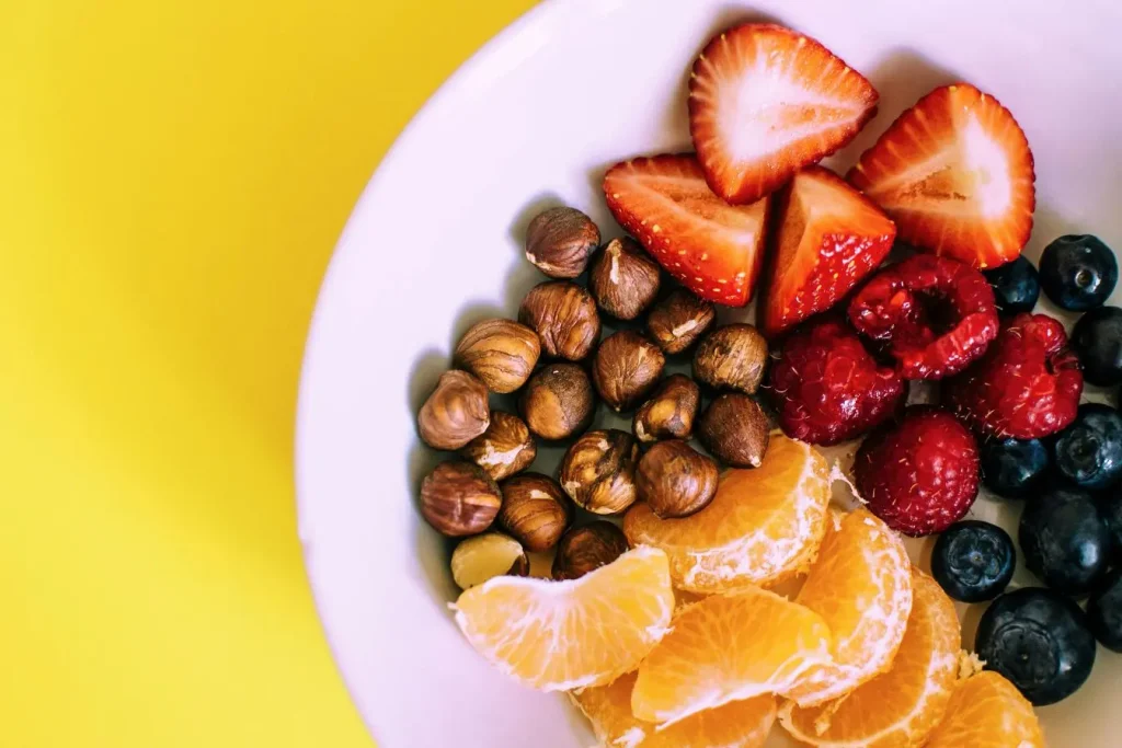 Bol blanc rempli de fraises, framboises, myrtilles et oranges reflétant la vitalité et l’énergie apportées par la vitamine D.