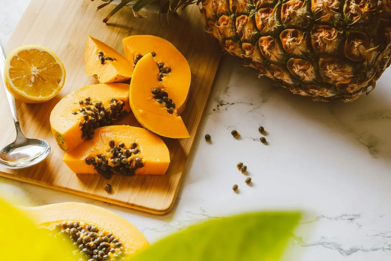 Fruits tropicaux Tranches de papaye orange avec graines noires sur planche en bois, image illustrant les enzymes digestives naturelles présentes dans les fruits tropicaux.