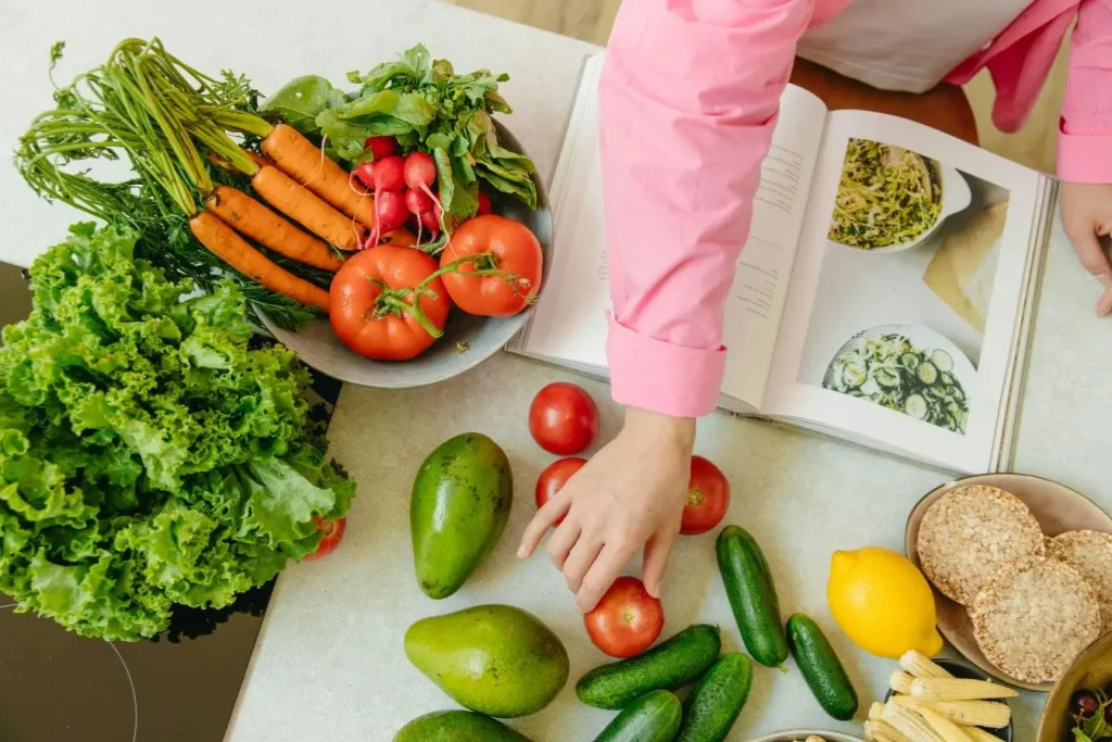 Plan de travail avec légumes frais, fruits colorés et livre de recettes, illustrant l’alimentation végane et santé au quotidien.