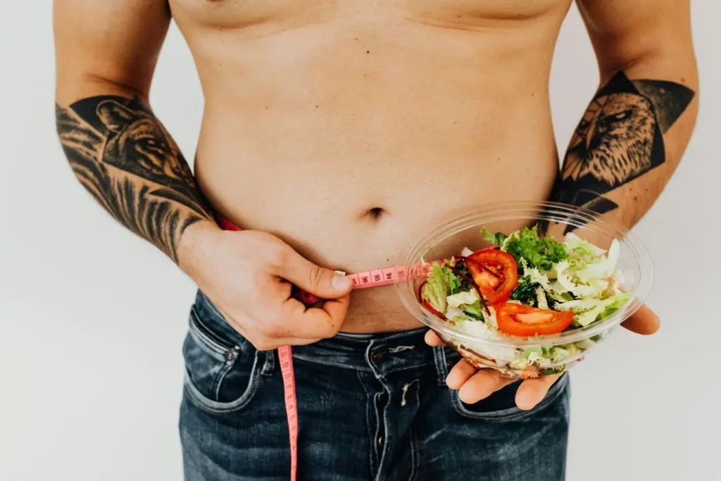 Scène santé, un mètre rose mesure la taille tandis qu’un bol de salade est tenu, visuel pratique pour montrer le régime cétogène.