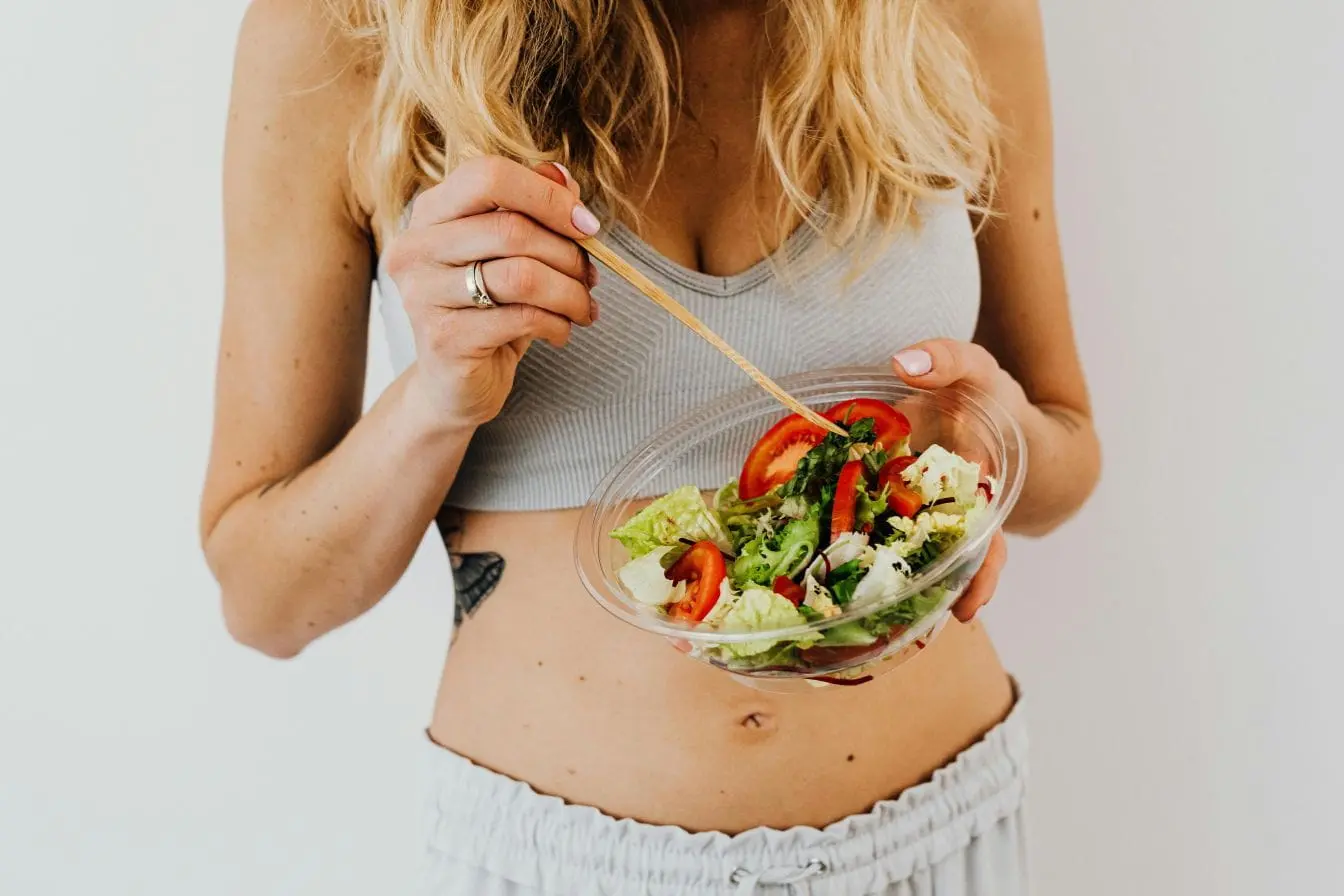 Femme tenant bol de salade fraîche avec baguettes, image illustrant le lien entre alimentation équilibrée et fertilité féminine.