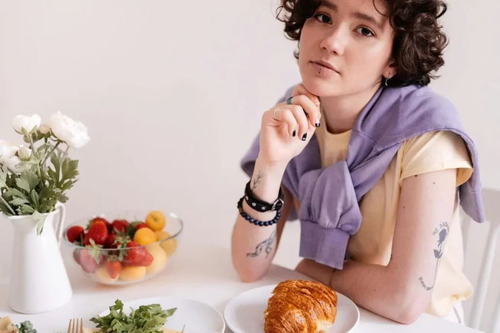 Personne assise à table avec croissant et salade, image illustrant l’alimentation intuitive basée sur plaisir et écoute des besoins corporels.