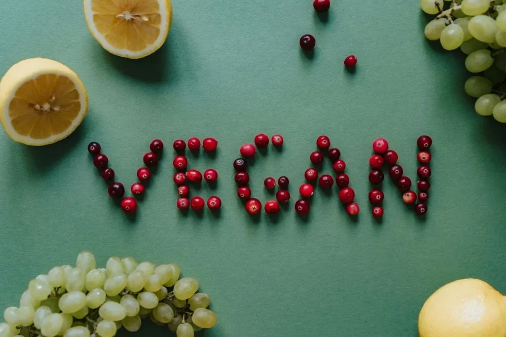 Mot VEGAN formé avec baies rouges sur fond vert entouré de citrons et raisins, illustrant l’alimentation végane et santé naturelle.