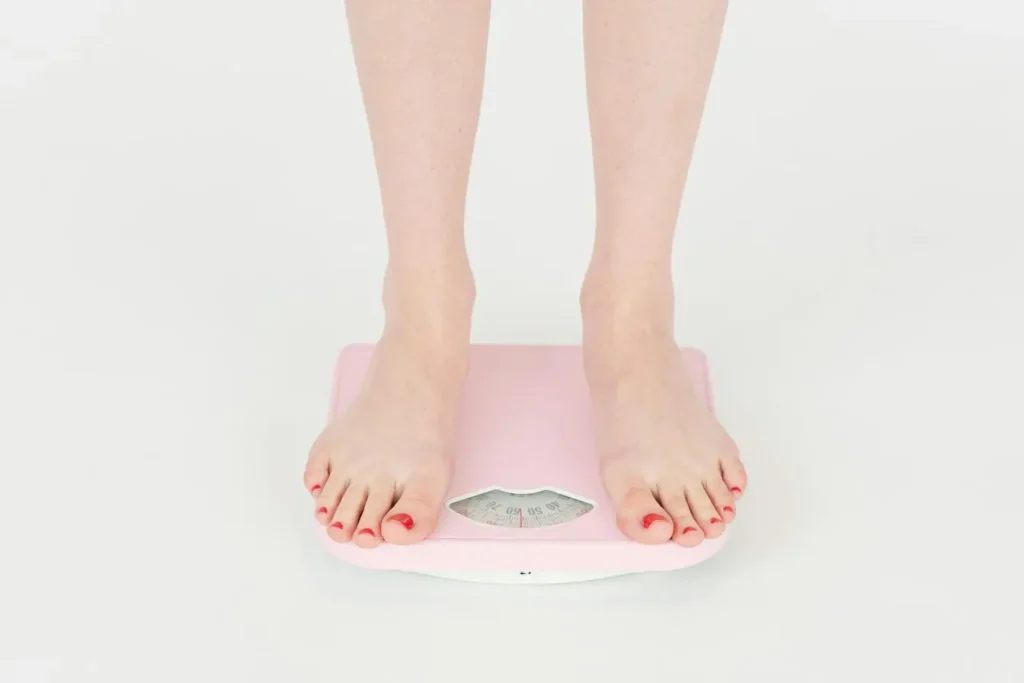 Personne debout sur balance rose montrant comment le stress quotidien peut influencer le poids corporel.