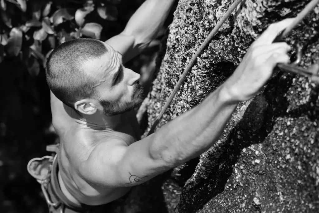 Grimpeur torse nu accroché à paroi rocheuse, image illustrant l’escalade et les muscles sollicités.