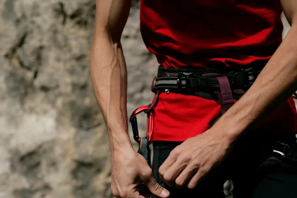 Gros plan sur grimpeur ajustant harnais noir, image illustrant l’escalade et les muscles sollicités.