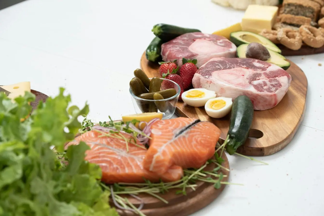 régime cétogène Plateau en bois garni de saumon cru, viande rouge, œufs, avocat et fromages, image illustrant les aliments typiques d’un régime cétogène équilibré.