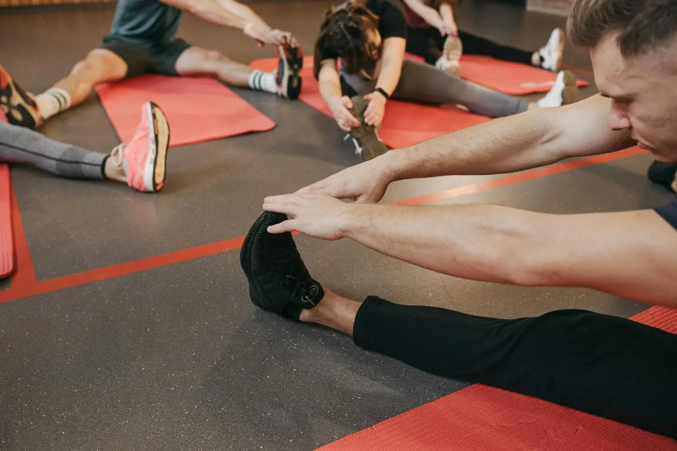 Groupe de personnes assises sur tapis rouges en salle de sport, image illustrant le stretching et l’assouplissement musculaire.