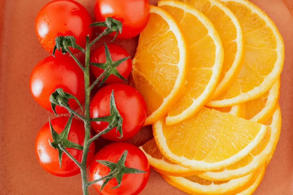 Grappe de tomates cerises fraîches avec gouttelettes d’eau posée près de tranches d’oranges, image illustrant l’intolérance à l’histamine et ses déclencheurs.