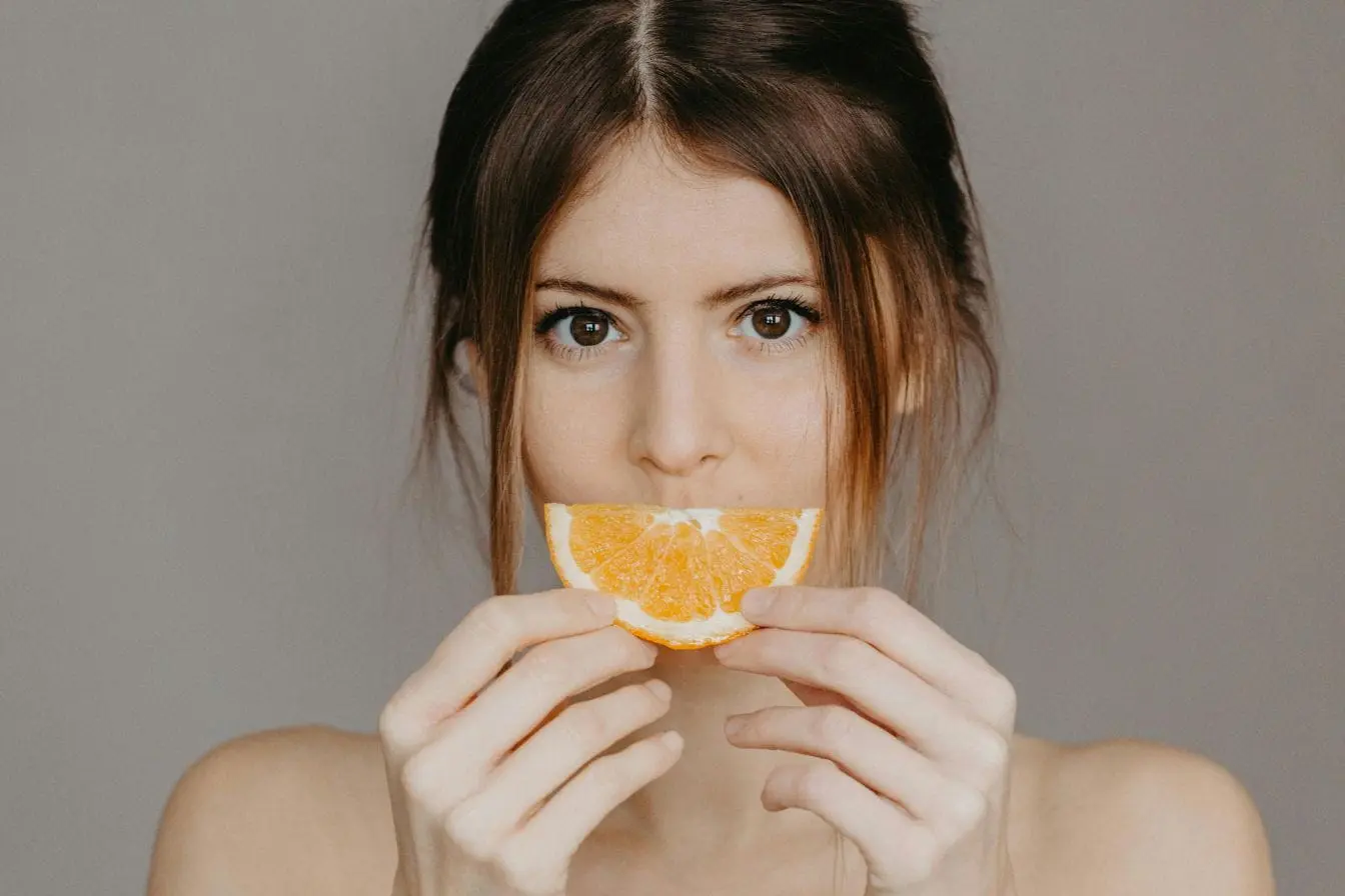 Personne tenant une tranche d’orange devant bouche reflétant l’importance de la vitamine D pour la vitalité et le bien-être.