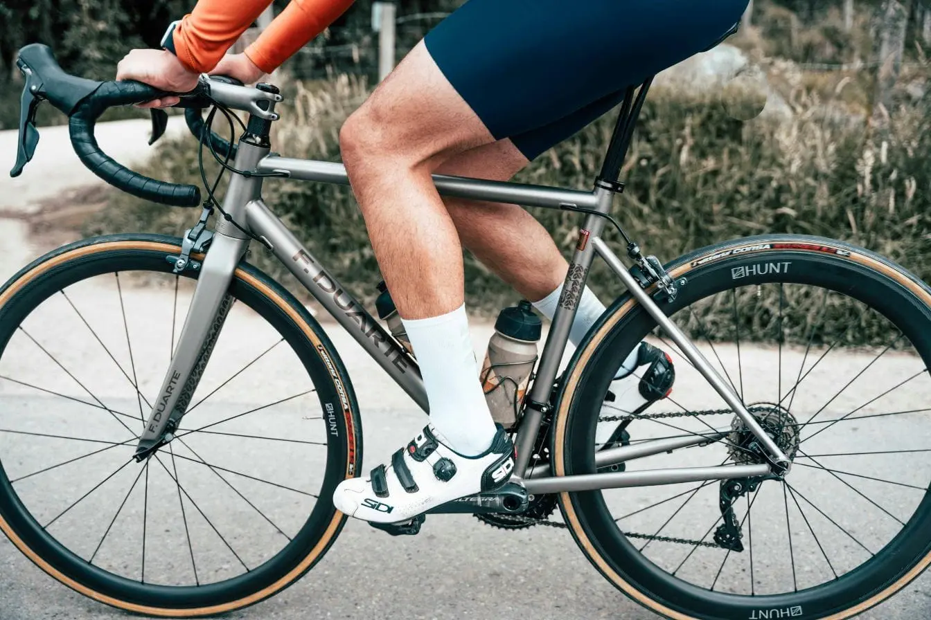 Cycliste en maillot orange pédalant sur vélo gris, image représentant les muscles sollicités lors du vélo de route et leur rôle dans l’effort.
