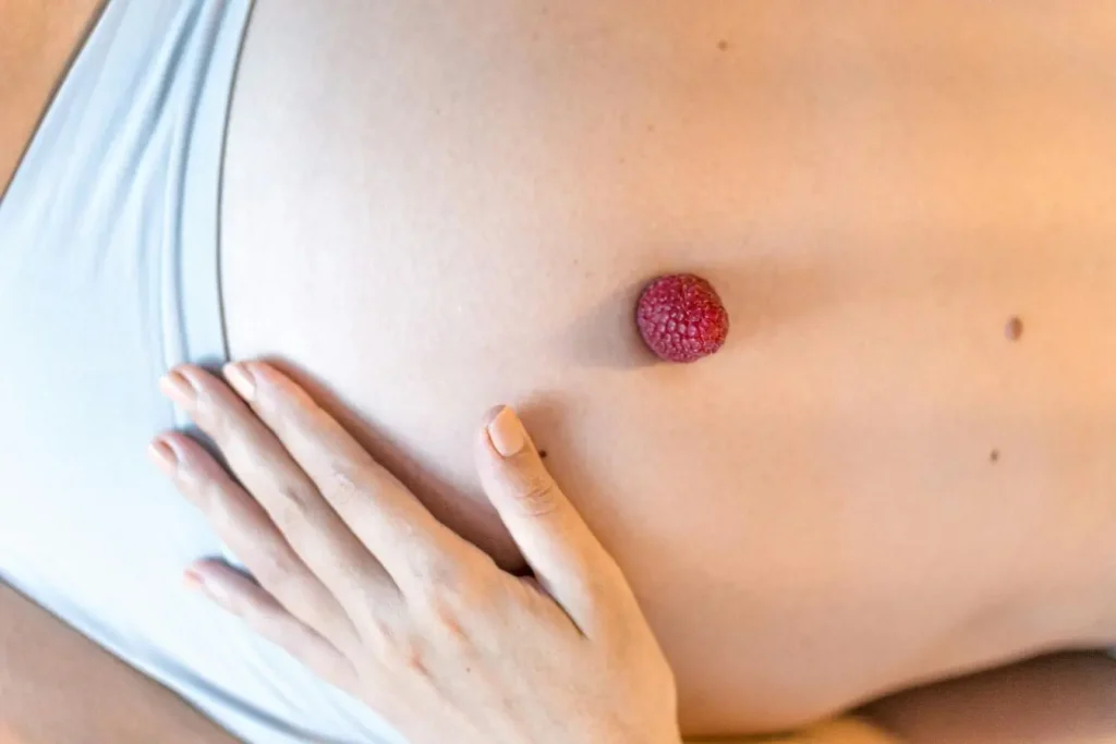 Gros plan sur ventre féminin avec framboise posée, image illustrant le lien entre alimentation saine et fertilité féminine.