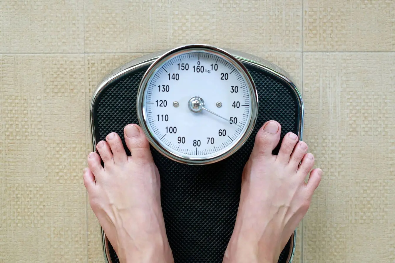 Pieds sur balance affichant 55 kg, image illustrant le lien entre rythme circadien perturbé et prise de poids progressive.