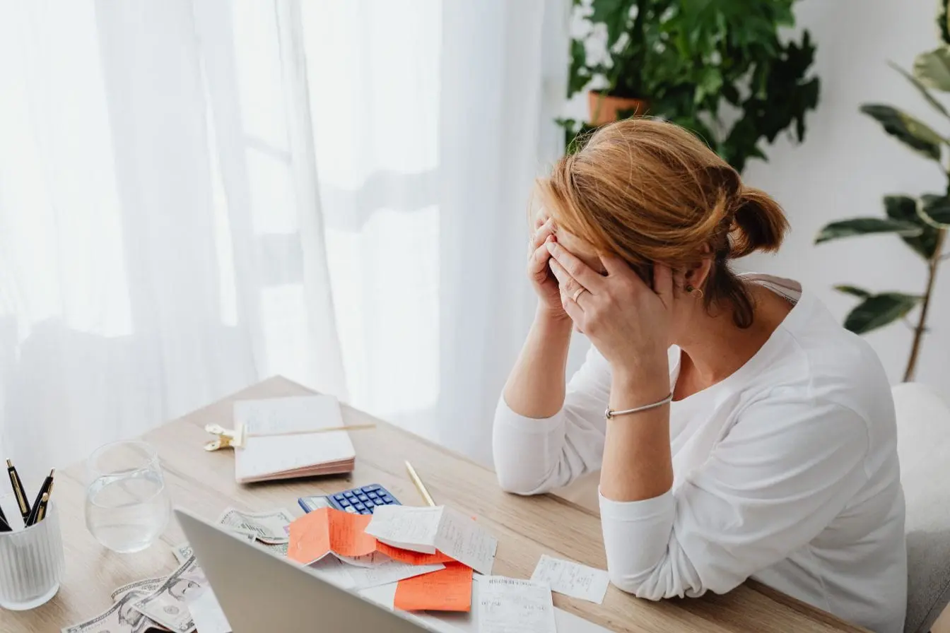 Personne assise au bureau, mains sur le visage devant papiers et reçus, image qui illustre l’impact de l’alimentation sur la concentration adulte.