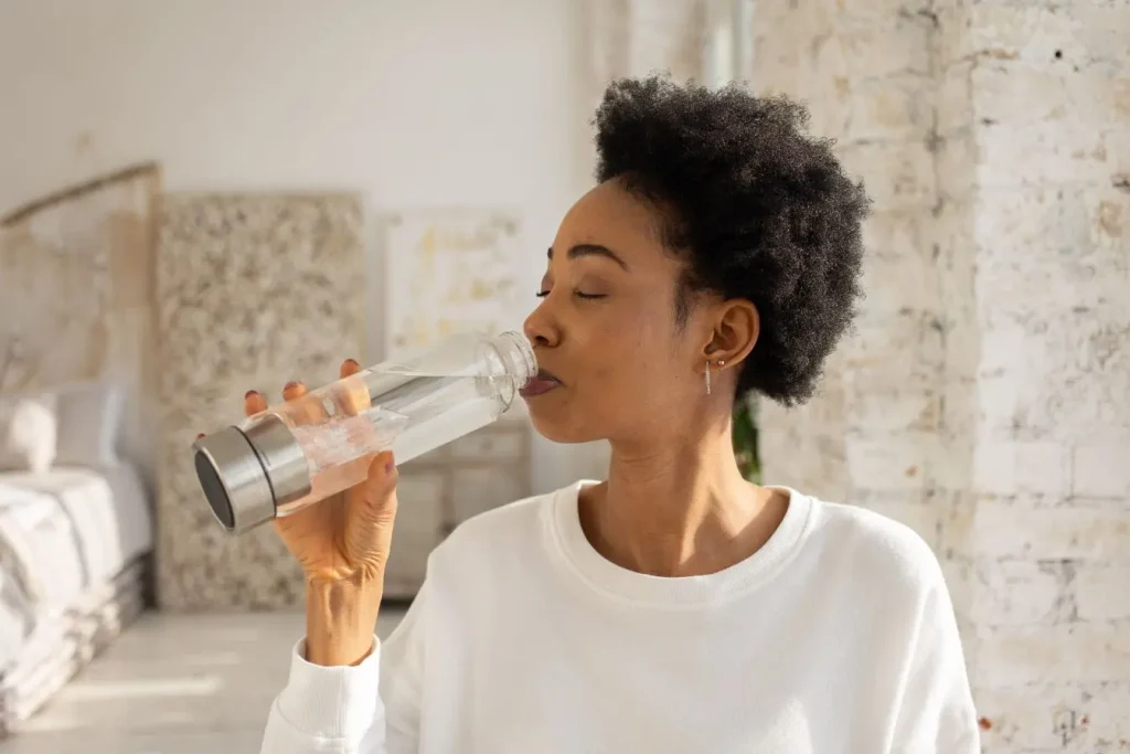 Personne buvant de l’eau claire dans une chambre lumineuse, image qui illustre l’importance de l’hydratation et de l’alimentation contre la dépression saisonnière.