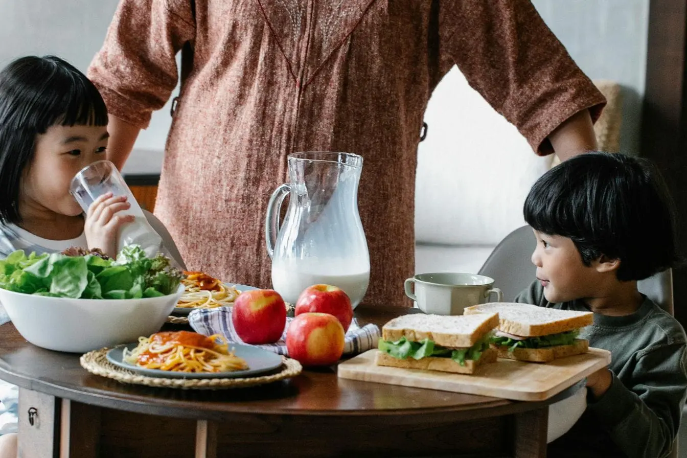 alimentation équilibrée adaptée aux enfants Deux enfants assis à table avec assiettes de pâtes et salade, image illustrant une alimentation équilibrée adaptée aux enfants de 3 à 6 ans.