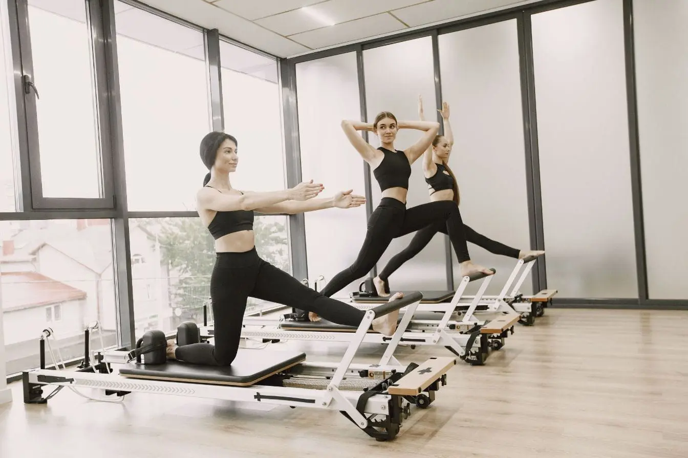 machines Pilates Trois personnes en tenue noire pratiquent des exercices sur machines Pilates, image qui illustre la progression visible sur le corps après quelques semaines.